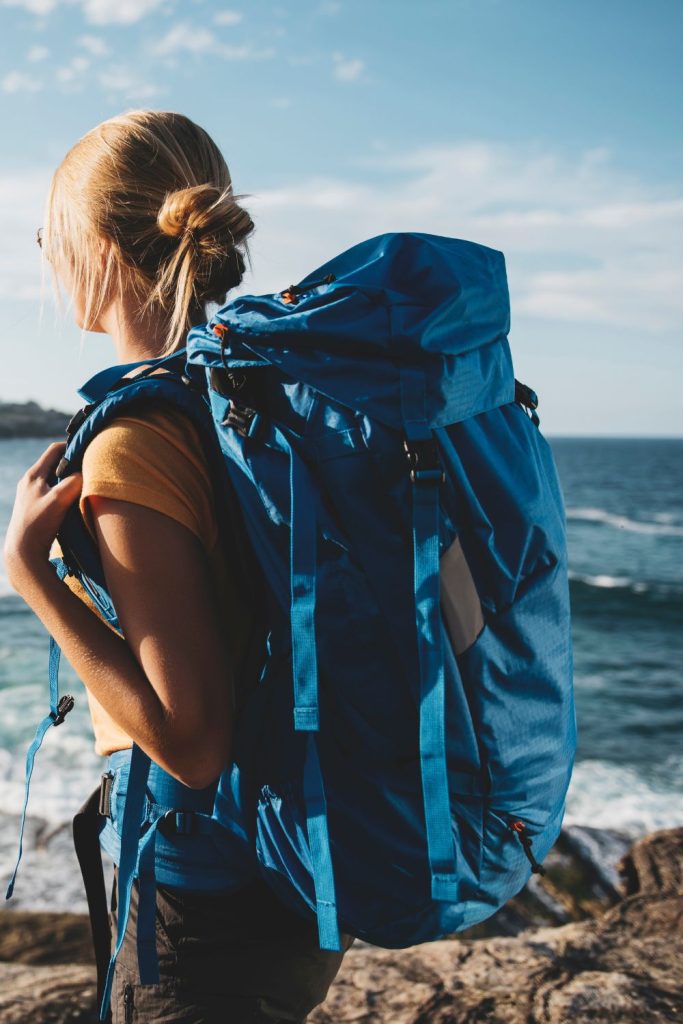 backpacking around the world - woman with blue backpack next to ocean
